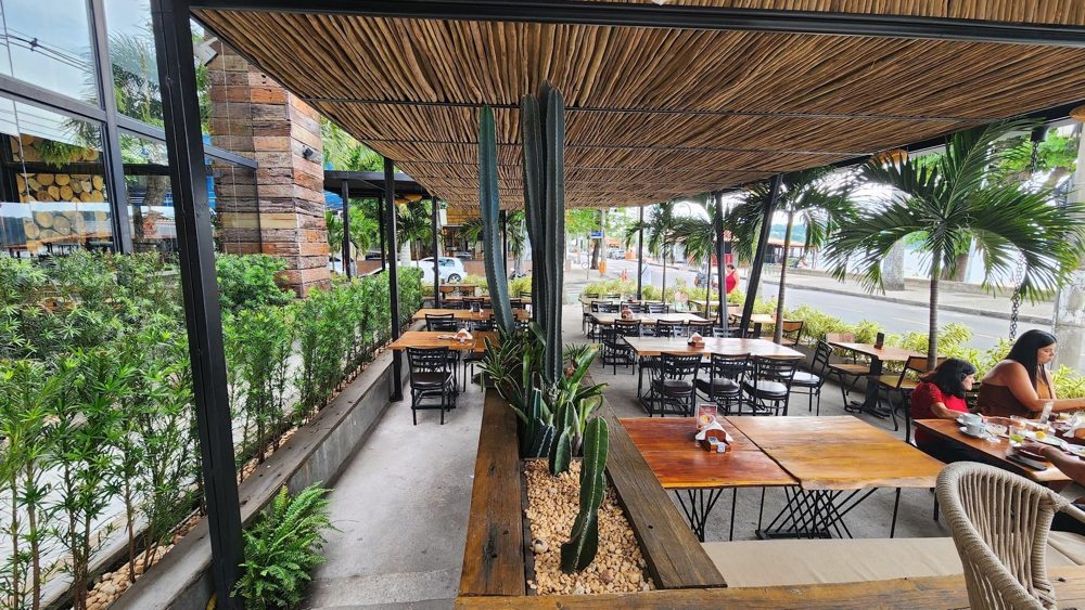 Varanda coberta do restaurante com mesas, vegetação e clientes